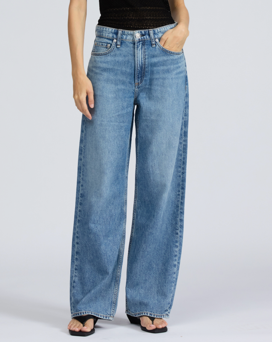 A person wears Rag & Bone's Featherweight Logan Wide jeans in light blue with a black sleeveless top and black sandals, standing against a plain light background.