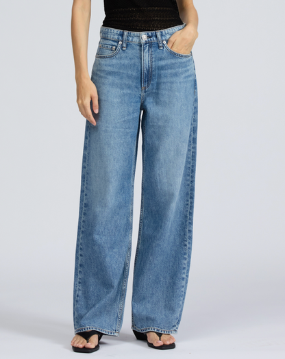 A person wears Rag & Bone's Featherweight Logan Wide jeans in light blue with a black sleeveless top and black sandals, standing against a plain light background.