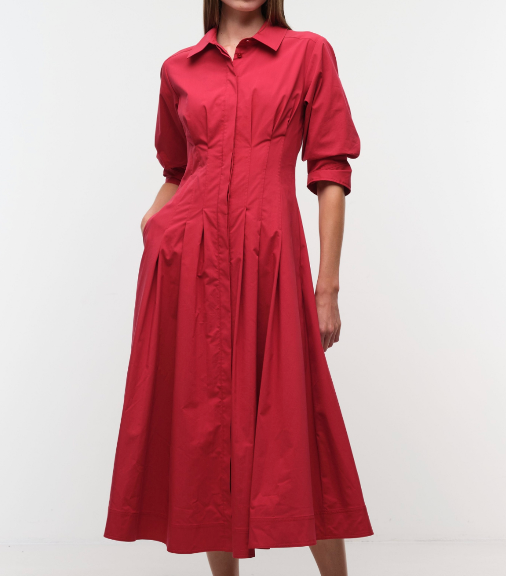 Woman wearing the Simkhai Jazz Pintuck Midi Dress—a long-sleeved, collared, red cotton poplin dress with a fitted waist and pockets—against a white background.
