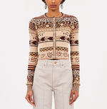 A person wears the Ulla Johnson Liza Cardigan, a patterned, long-sleeve button-up with Fair Isle earth-tone motifs, paired with high-waisted light beige pants.