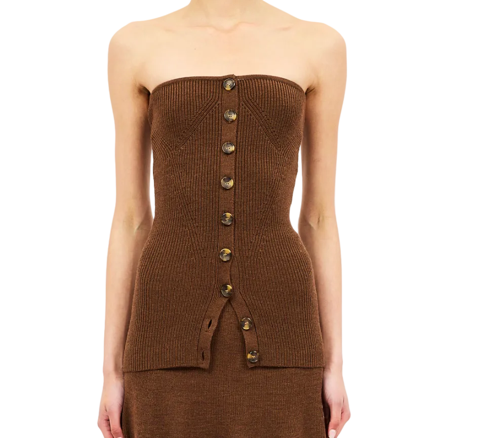 A person wearing the Ulla Johnson Yanni Strapless Knit Top, a brown ribbed knit tube top featuring front button detailing. The upper part of the skirt is also visible against a white background.