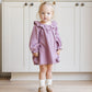 A young blond girl with pigtails stands indoors in front of a white cabinet, wearing the Quincy Mae Baby Girls' and Girls' Long Sleeve Isla Dress with white socks and tan shoes.
