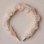 Noralee’s Gathered Headband features sheer, ruffled material with delicate sequins—perfect for special occasions. Shown on a light textured surface.