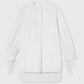The CO Cuff Tie Shirt is a long-sleeved white blouse featuring a round neckline, henley placket, extended hem, and ribbon ties at the cuffs.