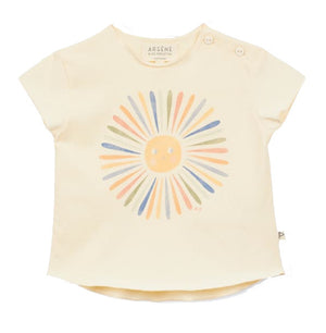 The Arsene & Les Pipelettes Baby Girls' Fleur T-Shirt is a cream-colored children's top made from soft organic cotton, featuring a pastel sun graphic and two buttons on the left shoulder.