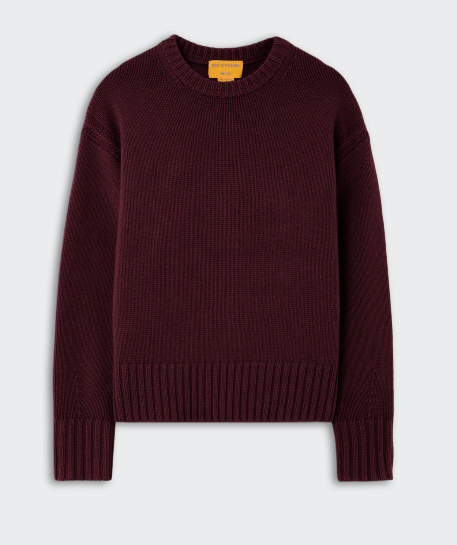 The Guest in Residence Cozy Crew Cashmere Sweater is a plain, long-sleeve, dark burgundy knit featuring ribbed cuffs, hem, and neckline, with a classic cozy crew silhouette laid flat against a light gray background.