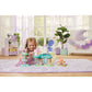 A young girl kneels on a purple rug, playing with the Calico Critters Woodland Wonder Fairy Castle in a bright, neatly decorated room with plants and pastel furniture.
