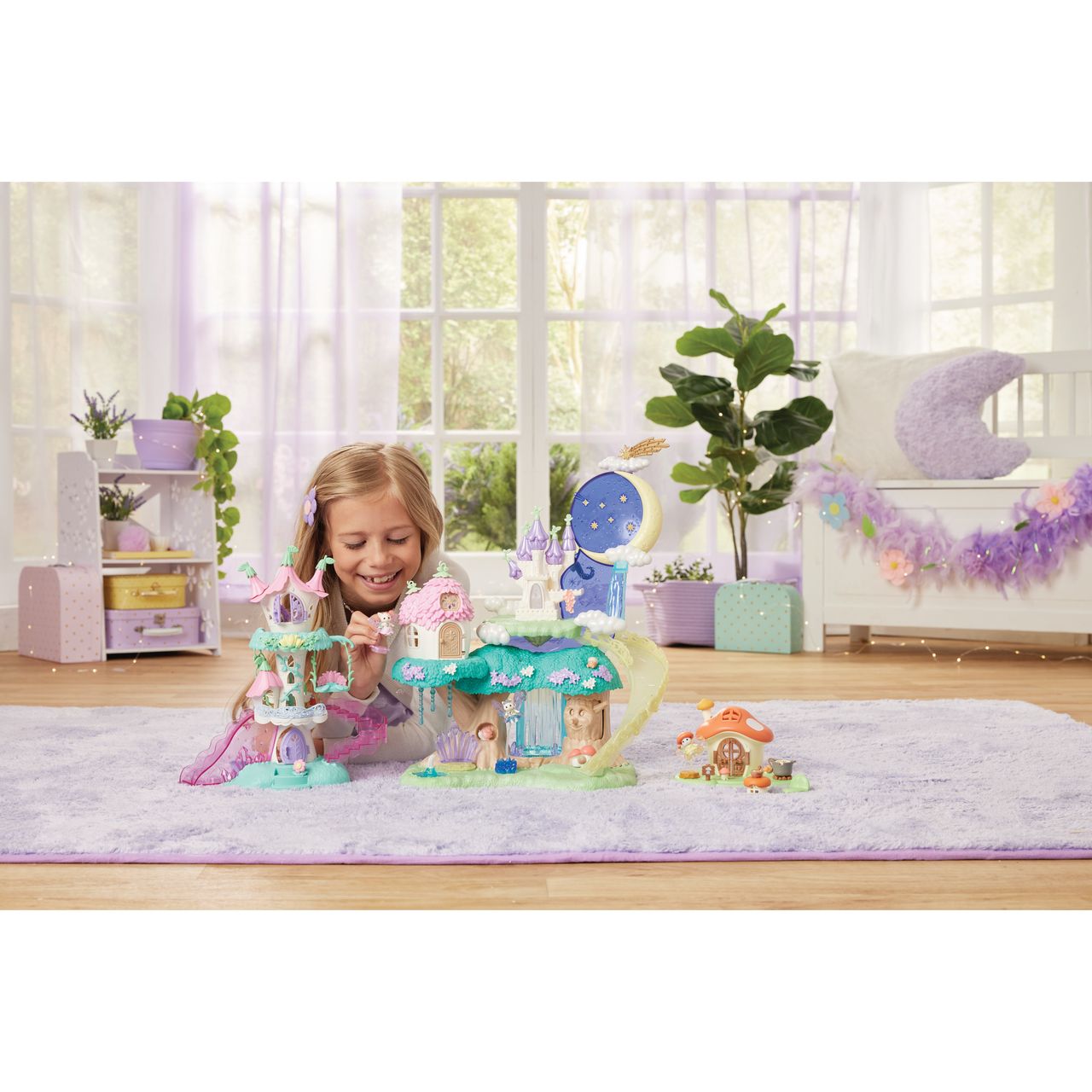 A young girl kneels on a purple rug, playing with the Calico Critters Woodland Wonder Fairy Castle in a bright, neatly decorated room with plants and pastel furniture.