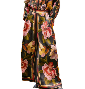 A person wearing Farm Rio's Chenille Flowers Black Pants, featuring large colorful floral patterns, vertical stripes, a relaxed fit, and hands in the pockets.