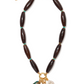 The Marilla Necklace by Lizzie Fortunato is a statement piece with large dark oval beads, green spacers, a gold chain, and five assorted charms—pearl, gold coins, and a black heart.