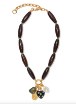 The Marilla Necklace by Lizzie Fortunato is a statement piece with large dark oval beads, green spacers, a gold chain, and five assorted charms—pearl, gold coins, and a black heart.