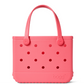 A vibrant pink, rectangular Bitty Bogg® Bag by Bogg Bags, featuring two sturdy handles and several circular holes on the front. This compact tote is washable, and “bogg” is embossed in the bottom right corner.
