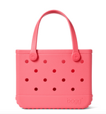 A vibrant pink, rectangular Bitty Bogg® Bag by Bogg Bags, featuring two sturdy handles and several circular holes on the front. This compact tote is washable, and “bogg” is embossed in the bottom right corner.