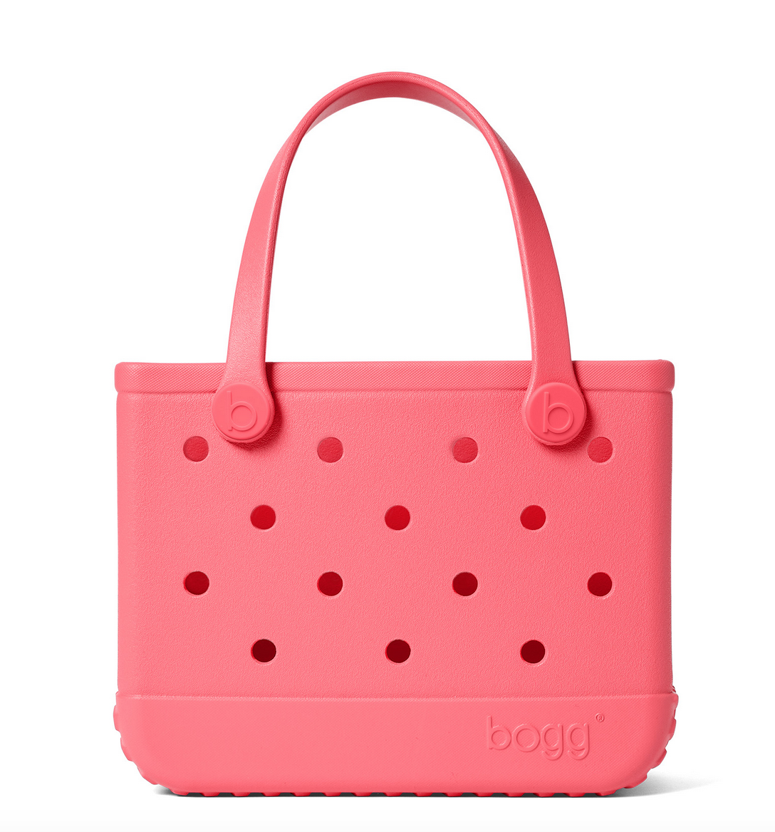 A vibrant pink, rectangular Bitty Bogg® Bag by Bogg Bags, featuring two sturdy handles and several circular holes on the front. This compact tote is washable, and “bogg” is embossed in the bottom right corner.