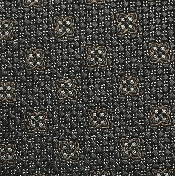 Close-up of the Robert Jensen Clover Pattern Tie, handcrafted by California Central Coast artisans, featuring a geometric motif of brown and white four-petaled flowers on a dark background.