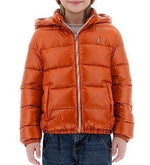 A child wearing the Herno Kids' Nylon Ultralight Hooded Jacket in orange, made from ultralight nylon fabric, is standing and smiling. This water-resistant jacket by Herno features a front zipper and two side pockets, providing both practicality and a luxurious feel.