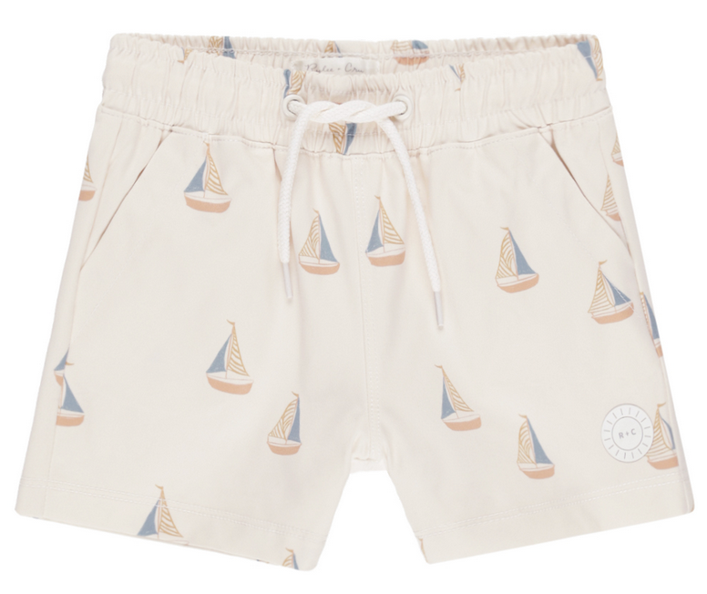 The Rylee & Cru Boys' Board Short features a beige color, elastic waistband, drawstring, and a blue and tan sailboat print—perfect for pairing with a matching swimsuit.