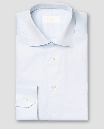 The Eton Solid Elevated Twill Shirt, featuring a spread collar and white buttons, is crafted from luxurious twill fabric in light blue and shown folded against a plain light gray background.