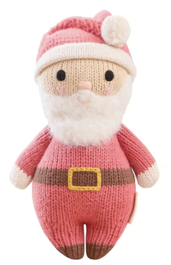 Introducing Baby Santa by Cuddle + Kind—a delightfully soft knitted doll featuring a red hat, white beard, rosy cheeks, and a yellow-buckled belt, shown against a white background. The perfect holiday companion for cozy baby snuggles.