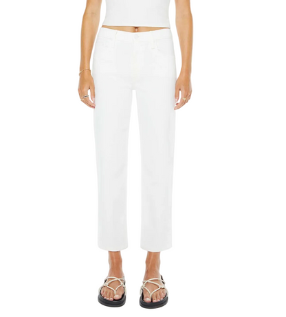 A person wears The Newbie Ankle high-rise stretch denim jeans by Mother, paired with a white crop top and black sandals, standing against a plain background.