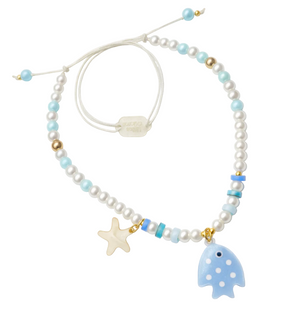 The Fish Blue Necklace by Lillies & Roses features white, blue, and gold beads with a starfish charm, iridescent pearls, and a blue fish pendant, all strung on an adjustable white cord.