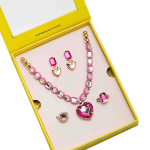 A yellow box from Super Smalls displays the Perfectly Pink Mega Set, featuring play jewelry including a gemstone heart pendant necklace, pink stud earrings, gold heart earrings, a pink gem ring, and a round pink gem brooch inside.