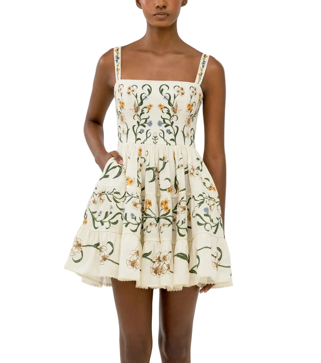 A woman wears the Lima Mini Dress by Agua By Agua Bendita, a sleeveless cotton mini with a square neckline, floral print, and tiered A-line silhouette above the knee.