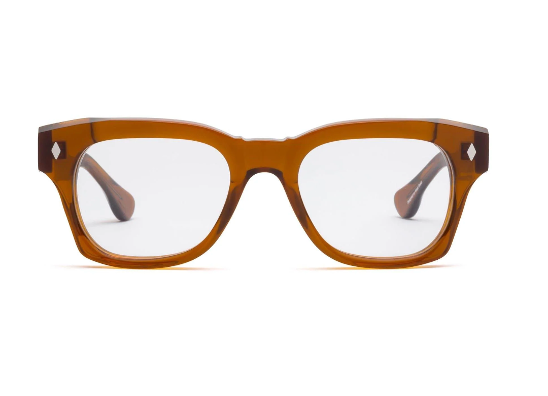 The Caddis Muzzy Reader features thick, transparent brown bio-based acetate rectangular frames and clear, scratch-resistant lenses, shown facing forward against a white background.