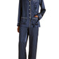 Wearing the Olivia von Halle Coco Silk Pajamas, this person models a navy silk set featuring distinctive white piping, a button-up long-sleeve top, and full-length pants. Standing barefoot against a plain background, they showcase an elegant evening look that effortlessly blends classic style with luxurious comfort.
