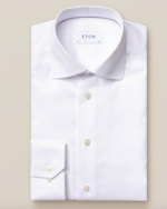 A folded White Signature Twill Shirt, Slim Fit by Eton is showcased on a beige background. It features a spread collar and buttoned cuffs, making it ideal for business meetings by keeping you sharp and wrinkle-free all day long.