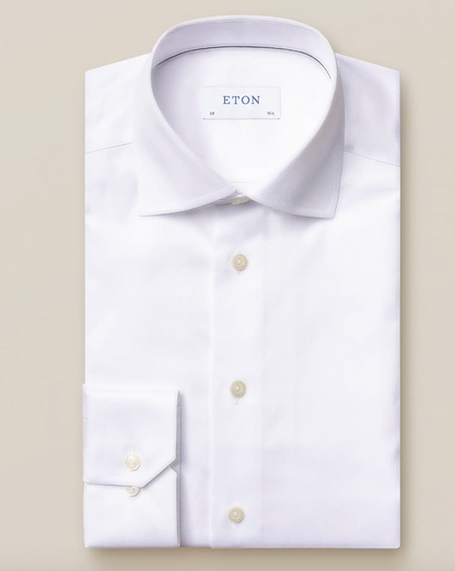 A folded White Signature Twill Shirt, Slim Fit by Eton is showcased on a beige background. It features a spread collar and buttoned cuffs, making it ideal for business meetings by keeping you sharp and wrinkle-free all day long.