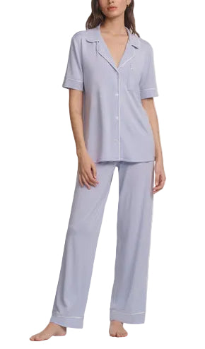 A woman stands barefoot wearing the Eberjey Gisele Short Sleeve Long Pant PJ Set—a light blue, classic fit pajama with short sleeves and matching straight leg pants featuring an elastic waistband.