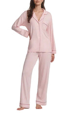 A woman wears the Eberjey Gisele Long PJ Set, a light pink long sleeve button-front top with straight leg pants, standing barefoot with one hand on her hip.
