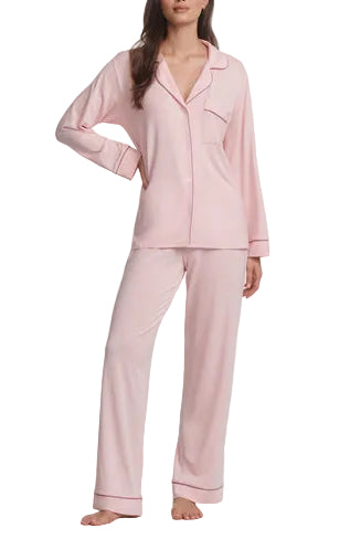 A woman wears the Eberjey Gisele Long PJ Set, a light pink long sleeve button-front top with straight leg pants, standing barefoot with one hand on her hip.