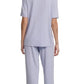A person stands barefoot facing away, wearing the Eberjey Gisele Short Sleeve Long Pant PJ Set in light purple, featuring a classic fit top and matching straight leg pant with an elastic waistband.