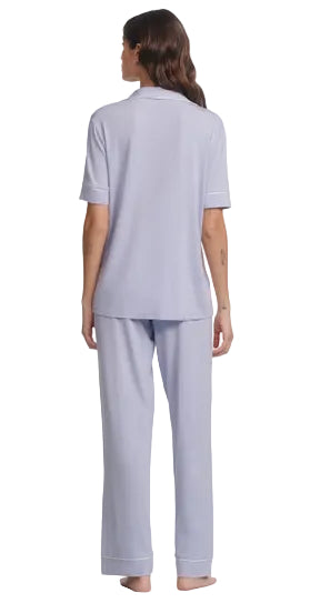 A person stands barefoot facing away, wearing the Eberjey Gisele Short Sleeve Long Pant PJ Set in light purple, featuring a classic fit top and matching straight leg pant with an elastic waistband.