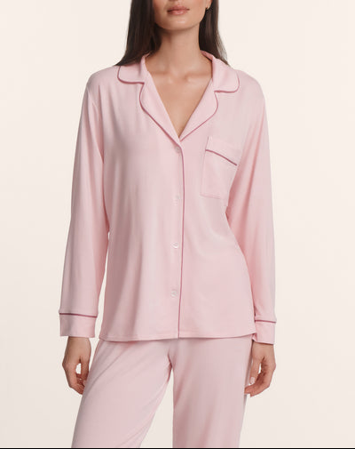A woman wears the Eberjey Gisele Long PJ Set: a light pink, long-sleeve button-front top with collar and chest pocket, paired with matching straight-leg pants.