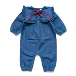 The Baby Girls’ Celiciane Romper by Louis Louise features blue chambray fabric with long sleeves, a sailor collar adorned with a ruffled edge and red bow, and charming small red heart prints on the chest; it also offers a convenient snap inseam for easy changing.