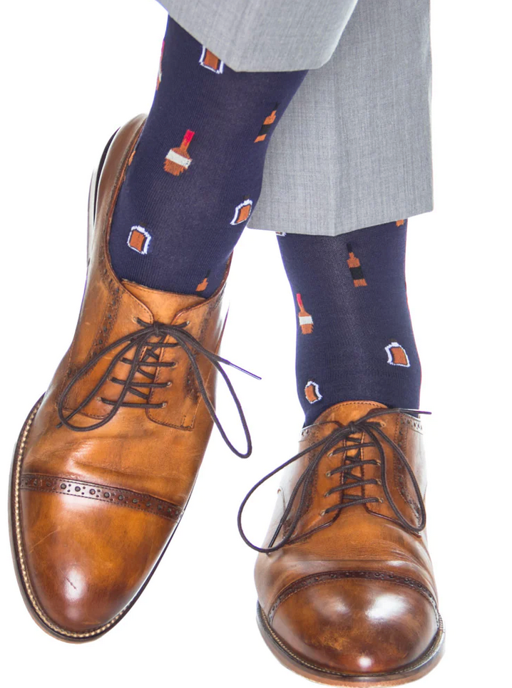 Brown leather dress shoes and gray pants paired with Dapper Classics Bourbon Bottle Mid Calf Socks in classic navy and burnt orange, made of fine mercerized cotton, featuring brown and red bottle patterns.