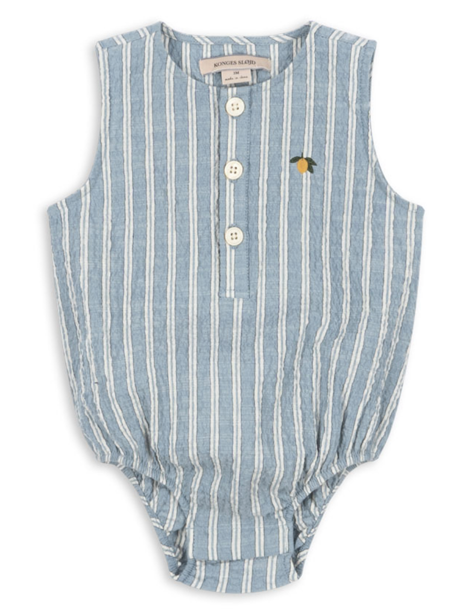 The Baby Boys’ Elliot Romper by Konges Slojd features blue and white vertical stripes in a sleeveless seersucker design, three front buttons for easy diaper changes, elastic leg openings, and a small embroidered lemon detail near the chest.