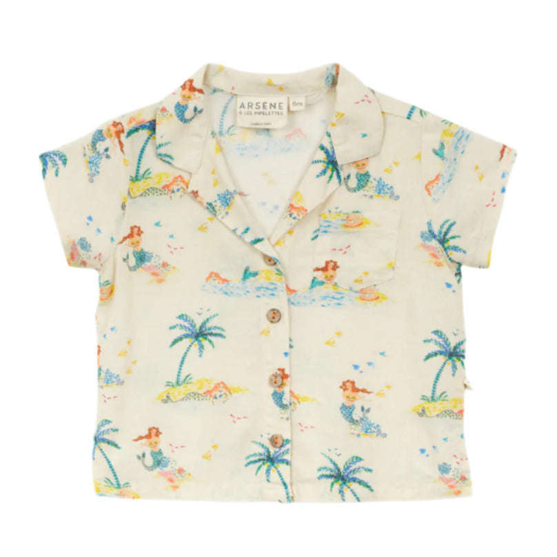 The Arsene & Les Pipelettes Baby Girls' Flynn Shirt is a cream short-sleeve top featuring a playful mermaid, palm trees, swimmers print, button-down front, and notched collar.