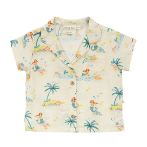 The Arsene & Les Pipelettes Baby Girls' Flynn Shirt is a cream short-sleeve top featuring a playful mermaid, palm trees, swimmers print, button-down front, and notched collar.