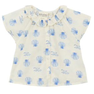 The Arsene & Les Pipelettes Baby Girls' Felixia Top is a white short-sleeve blouse with a blue shell and wave print, ruffled collar, and front buttons.