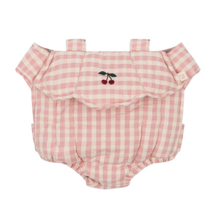 The Konges Slojd Doll Carrier is an adorable infant romper featuring a pink and white checkered design with shoulder straps, cherry embroidery on the chest, and ruffled detailing around the neckline, making it perfect for doll parents to pack in a changing bag.