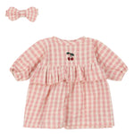 The Konges Slojd Doll Clothes Set by Konges Slojd includes a pink and white plaid baby dress crafted from organic cotton, featuring a cherry design on the chest, and comes with a matching bow headband. This set adheres to OEKO-TEX® STANDARD 100 standards.