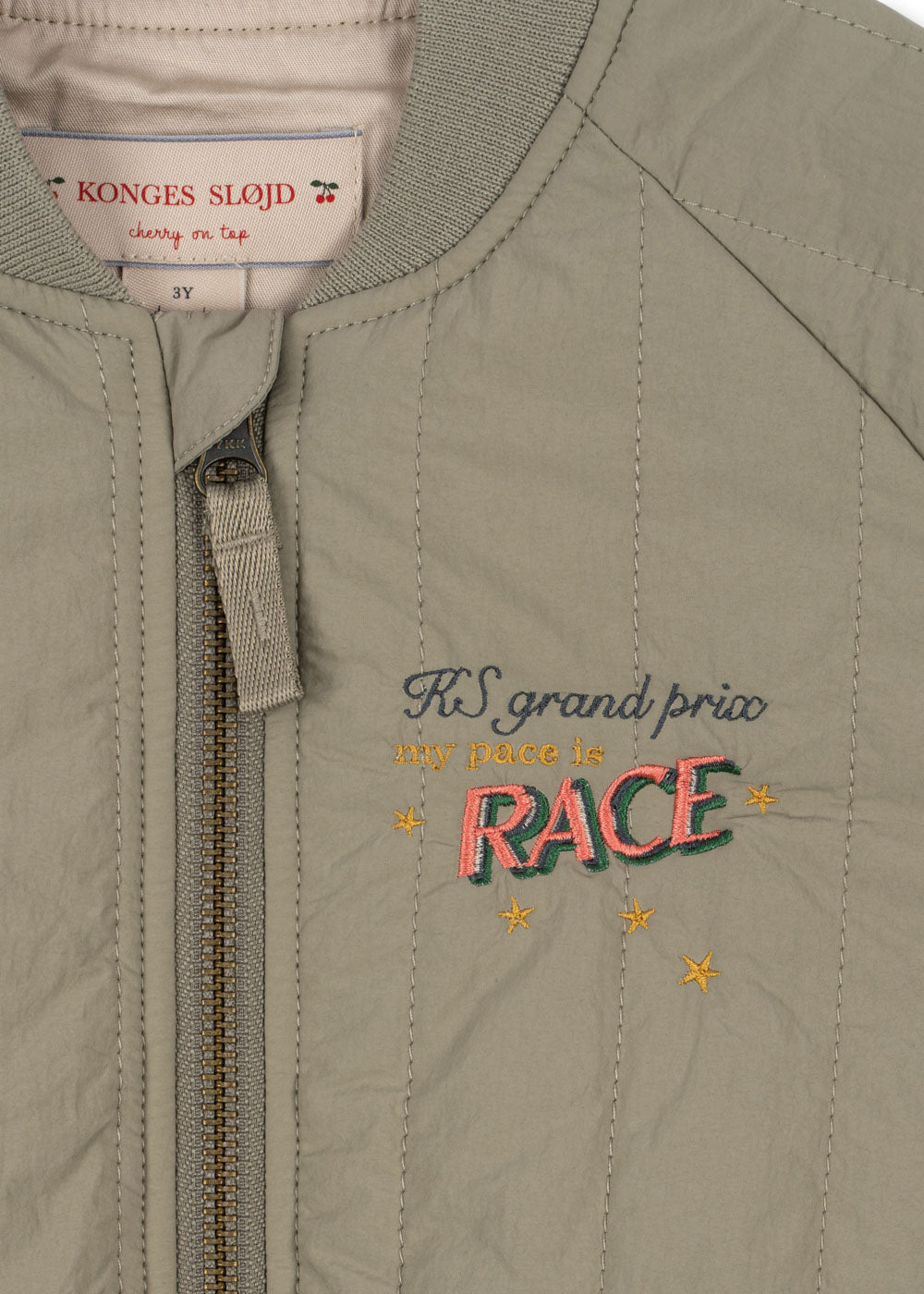 Close-up of the Konges Slojd Juno Bomber Jacket embroidered with "KS grand prix my pace is RACE." Made from water-repellent fabric, its label reads "Konges Sløjd cherry on top 3Y," providing style and superior insulation for chilly days.