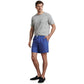 A man wears a grey t-shirt, Peter Millar Paloma Swim Trunk with four-way stretch and a subtle pattern, and black slip-on shoes, with one hand in his pocket.