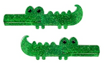 Two green, glittery crocodile-shaped objects with smiling faces and black eyes, positioned one above the other on a white background—these adorable pieces are the Lillies & Roses Alligator Glitter Hair Clips, charming nature-inspired hair accessories that double as playful glitter hair clips.