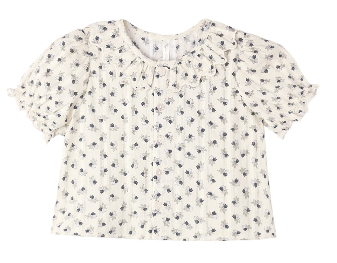 The Girls’ Liv Blouse by Rylee & Cru is a white short-sleeve button-down blouse featuring a scalloped, ruffled collar, small dark floral print, front button closure, and puffed sleeves.