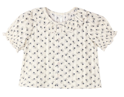 The Girls’ Liv Blouse by Rylee & Cru is a white short-sleeve button-down blouse featuring a scalloped, ruffled collar, small dark floral print, front button closure, and puffed sleeves.